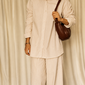 Person wearing a beige outfit with a brown bag against a plain background