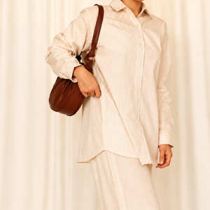 Person wearing a white outfit with a brown bag against a white curtain background