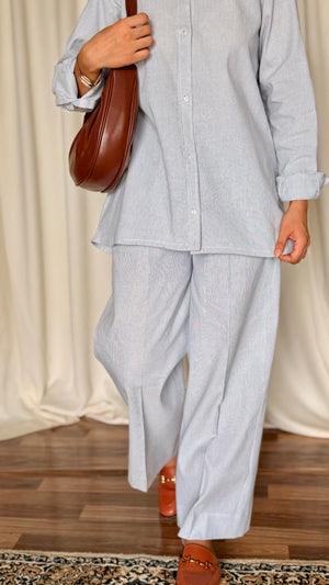 Person wearing a light gray outfit with a brown bag and shoes on a wooden floor.