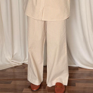 Person wearing a beige striped shirt and pants with a brown bag against a white curtain background