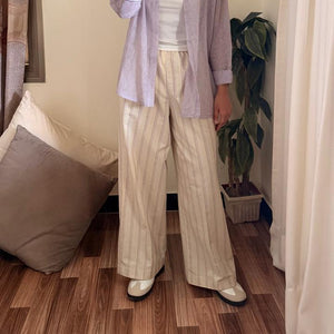 Person wearing a light purple shirt and beige pants in a room with a plant and framed picture on the wall.