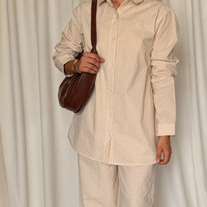 Person wearing a beige striped shirt and pants with a brown bag against a white curtain background