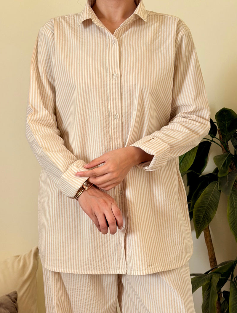 Person wearing a beige striped pajama set in a room with a plant and furniture.