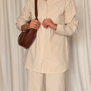Person wearing a beige striped shirt and pants with a brown bag against a white curtain background