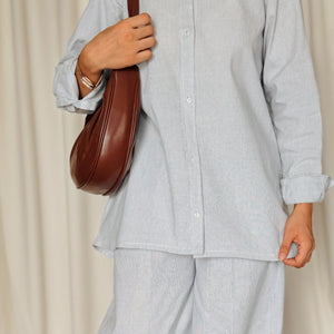 Person wearing a light gray outfit with a brown bag and shoes on a wooden floor.