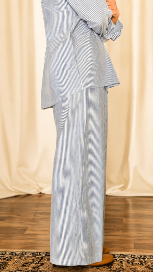 Person wearing a blue and white striped outfit against a beige curtain background