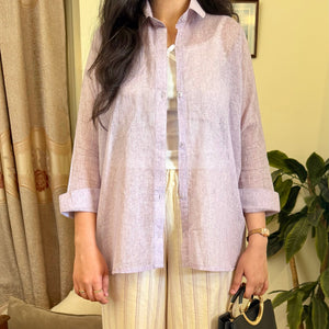 Woman in light-colored shirt and wide-leg pants holding a black handbag indoors.