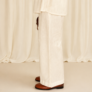 Person wearing a white outfit with a belt against a white curtain background