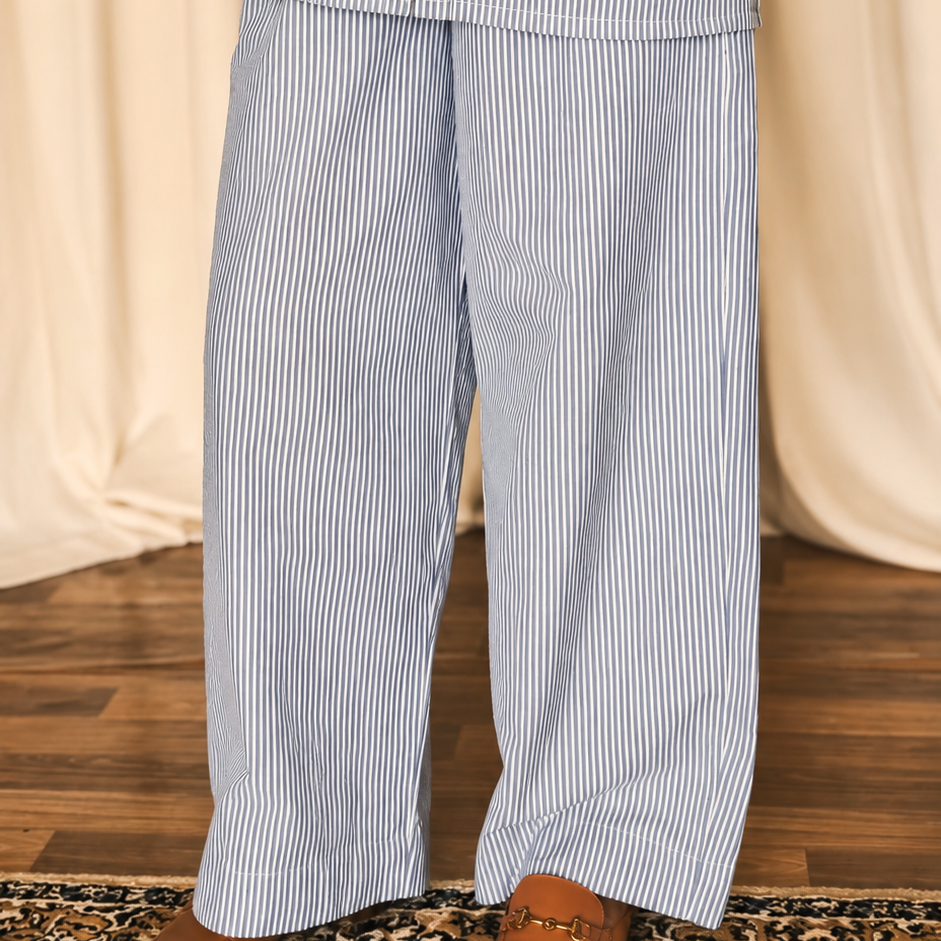 Person wearing blue striped pajamas holding a white mug against a beige curtain background